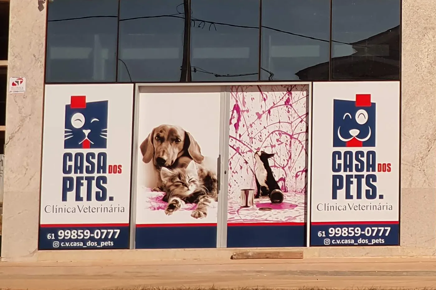 A fachada da Casa dos Pets, com as placas da clínica, o telefone e o Instagram nos vidros e as portas adesivadas com cão e gato.